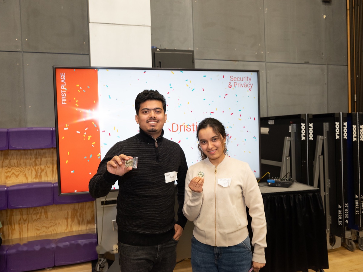 Two Dristi teammates holding first-place pins in front of a screen announcing Dristi as Security & Privacy track winner
